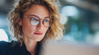 © Nuttawut - Focused Young Businesswoman with Glasses: A close-up portrait of a focused woman with glasses working on her computer.