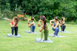 © Sirirat Makprasert - A group of women practicing yoga together on a lush green lawn, surrounded by trees, radiating peace, balance, and mindfulness in nature.