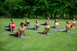 © Sirirat Makprasert - A group of women practicing yoga together on a lush green lawn, surrounded by trees, radiating peace, balance, and mindfulness in nature.