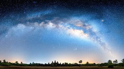 Wall Mural - A breathtaking panoramic night sky showcases the Milky Way galaxy arching over a dark silhouette of trees and ancient temple structures.
