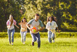 © Studio Romantic - Happy joyful young people friends in casual clothes playing with a ball on a green grass in the park outdoors. Men and women running on the lawn with ball and having fun in summer.