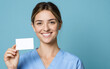 © Korkiat - Cinematic stock photo of a happy nurse holding up a business card against a blue background,
