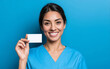 © Korkiat - A smiling nurse in blue scrubs holding up an empty business card, solid color background,