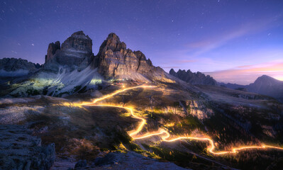 Wall Mural - car light trails on mountain road and high rocks at night in autumn in tre cime, dolomites, italy. c