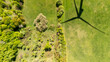© daily_creativity - Aerial view of a green landscape showing diverse vegetation with a wind turbine shadow casting over the ground, highlighting the harmony between nature and renewable energy.
