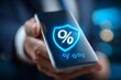 © Multiverse - Hand holding smartphone displaying security shield icon with percentage symbol in modern office environment