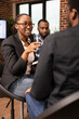 © DC Studio - Female business consultant with glasses provides financial advice to black man in brick wall office. African american woman manager discusses a company project while questioning her male employee.