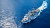 Military navy ship from aerial angle, crossing serene ocean waters with clear white wake, deck activity visible, sky reflected in the deep blue sea