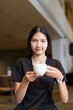 © Ranta Images - Young Asian woman sitting in coffee shop wearing black dress holding coffee cup