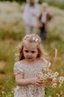 © looking2thesky - An adorable 3-year-old girl collects daisies in a wicker basket amidst a blooming field, radiating pure childhood joy and harmony with nature. Perfect for summer-themed and family content
