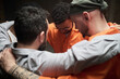 © pressmaster - Group of diverse men standing close together in circle embracing shoulders participating in group therapy session in prison setting showing support and unity