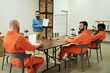 © pressmaster - Middle aged Caucasian man instructing three multiethnic male prisoners wearing orange jumpsuits during classroom lesson in prison