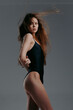 © SHOTPRIME STUDIO - Young woman in black swimsuit posing confidently against neutral gray background with long flowing hair and natural makeup, showcasing elegance and strength indoors.