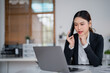 © MINAE - Young businesswoman is sitting at her desk, talking on her phone and working on her laptop, concentrating on her tasks in a bright and modern office environment