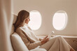 © anastasiiam - Businesswoman using tablet in luxury private jet cabin with soft natural light, beige tones, and quiet luxury aesthetic.