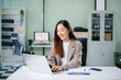 © laddawan - Confident young Asian businesswoman smiles while typing on her laptop at a modern office desk