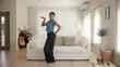 © ChayTee - Full length young adult active black asia people Gen Z woman enjoy relax move body happy fun dancer. Humor bizarre music funny dancing crazy joy playful mental at home sofa living room with pet dog.