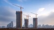 © intha - Three tall buildings under construction with cranes against a cloudy sky in an urban setting.