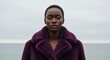 © Oleksandr - African female in purple coat posing outdoors near ocean under cloudy sky