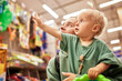 © Georgii - Young attractive woman with her cute baby in her hands walking around toy store. Beautiful mom and her little blonde daughter shopping in the mall and having fun. Family weekend, happy childhood.