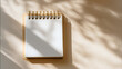 © Weiguo - Minimalist wooden desk with blank notebook under soft morning light, clean beige background.