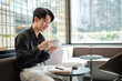 © wattana - Young man enjoying a warm drink in a cozy cafe lounge with notebook and smartphone on the table.