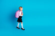 © deagreez - Cute schoolgirl walking with backpack on blue backdrop, showcasing school readiness, education concept, and childhood learning