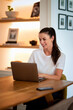 © sepy - Midle aged woman sitting at desk in her modern home and using a laptop computer