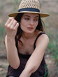 © Stanislav - Portrait of young woman in brown dress and straw hat sitting and relaxing against blur background of forest.
