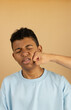 © Answer 7 - Vertical image of a Latino teenager wearing a light blue sweatshirt receiving a punch in the face on a light brown background, young man with a punch in the face
