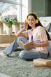 © Pixel-Shot - Beautiful young woman in headphones listening to audiobook with books and sitting on carpet in living room