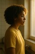 © Ulyana - Young african female in yellow shirt looking out window in warm light