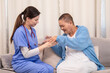 © Rakchanok - Nurse handing pill cup to senior woman, both engaging in daily care routine in cozy living room, showing empathy and support in elderly wellness, illness, healthcare, hosptality..