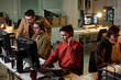 © pressmaster - Group of young people of diverse ethnicities working at computers with headsets, supervisor giving instructions, scam call center context