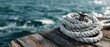 © Anastasia - The rope coiled on a weathered dock with tranquil water in the background.