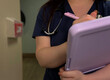 © Kelly - Nurse Writing on Clipboard in Hallway with Stethoscope Around Neck