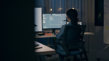 A dedicated female programmer seen from behind, intensely coding across multiple monitors in a dark office. Focuses on AI, machine learning, and software development.
