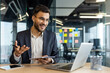 © Liubomir - A businessman in glasses smiles while talking on a video call in a modern office setting.