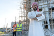 © Jack Tamrong - Arabic businessman standing arm crossed in construction site with blurred construction workers in site background