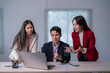 © Apichat - Three people are sitting at a desk with a laptop open in front of them