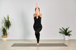 © TRAVELARIUM - Young caucasian woman performs eagle pose in minimalist yoga studio. She stands on one leg, focused and serene, surrounded by lush potted plants. Ambiance is calm and balanced