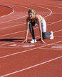 © Yevhen - Sportswoman crouching at the starting line, ready for a sprint on a red running track. Runner woman in sportwear getting ready to run sprint at low start on stadium track with red coated