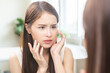 © KMPZZZ - Anti aging, worry puberty asian young woman, stressed girl looking in mirror, allergy presenting an allergic reaction from cosmetic on face. Beauty, health care from acne problem, dry skin, treatment.