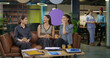 © Raushan_films - Indian asian smiling young adult gen z diverse girl woman sitting on sofa drink coffee indoor job office happy female intern staff talk funny gossip spend break time enjoy fun joy day at work place