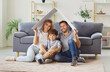 © Studio Romantic - Cheerful parents and son sit on the floor of home, holding a symbolic house roof over heads. This represents safety and protection in new home, celebrating family security and real estate.