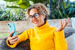 © simona - Curly-haired woman in her 40s using smartphone outdoors. Modern lifestyle with technology, chatting, calling, browsing, installing apps, staying connected and enjoying digital freedom on the go