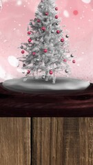 Wall Mural - animation of snow falling and glowing spots over snow globe with tree on pink background