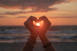 © Milou Dirks - silhouette of a pair of hands creating a heart on the beach near ocean with sun set in between