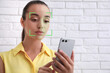 © New Africa - Woman unlocking her smartphone with facial recognition app indoors. Biometric verification