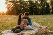 © La Famiglia - Happy couple enjoying romantic picnic in park at sunset, eating croissants and smiling
